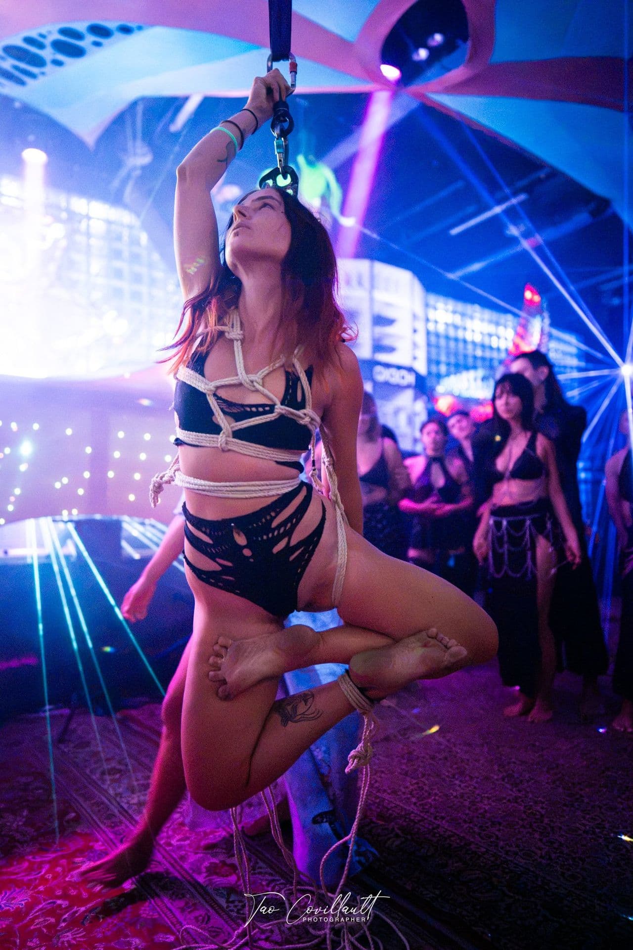 A rope performer suspended above the dancefloor among lasers