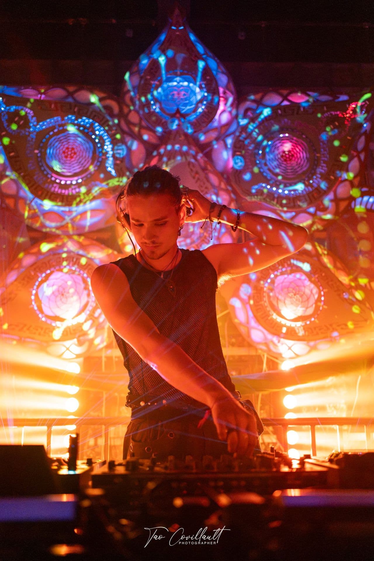 A DJ at the decks in front of a glowing orange mandala
